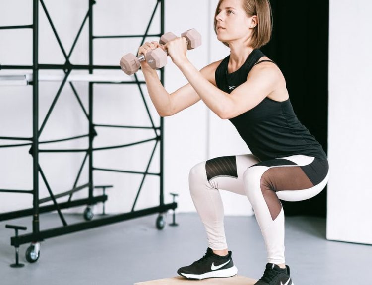 A woman in sportswear performs a squat with dumbbells indoors, embodying strength and healthy living.
