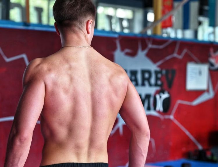Shirtless man showcasing muscular back indoors in fitness gym.